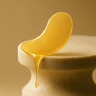 Glossy golden hydrogel eye patch with essence drip — texture close-up